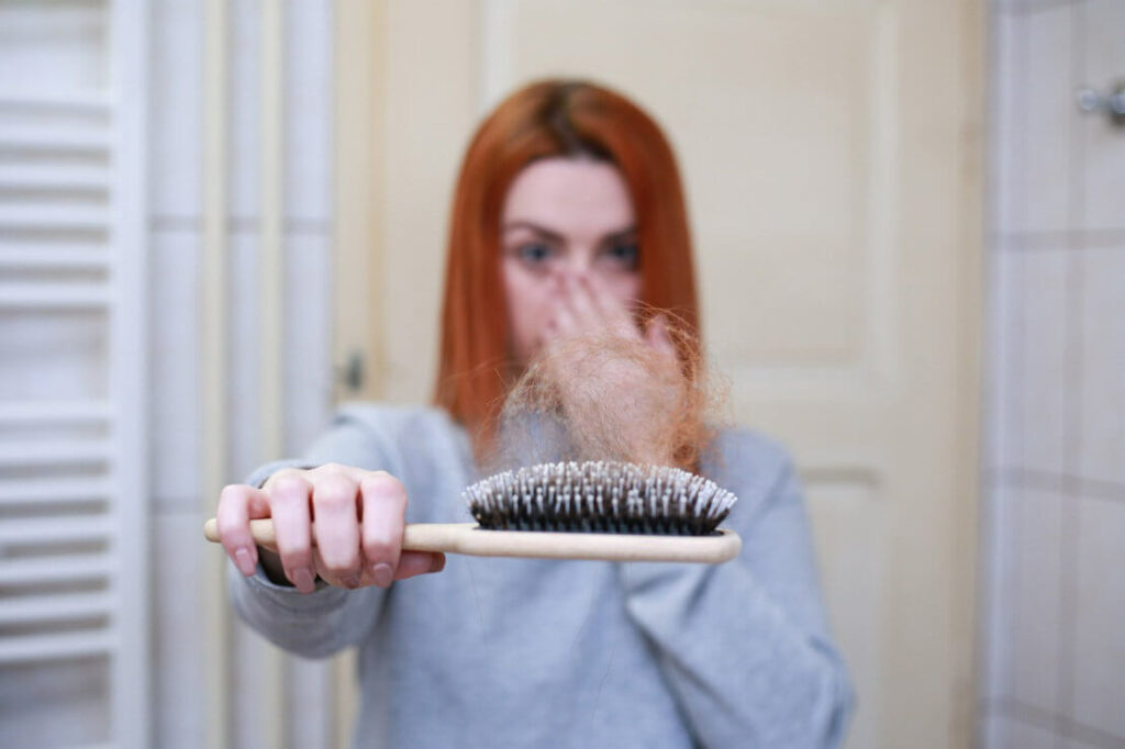 In the photo, a woman is holding a comb with red hair. The problem of hair loss also affects red-haired girls 